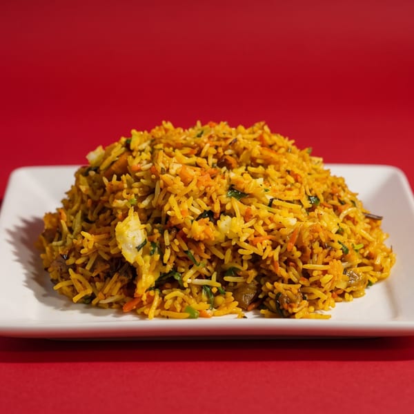 A large serving of yellow biryani rice with vegetables on a white rectangular plate against a red background.