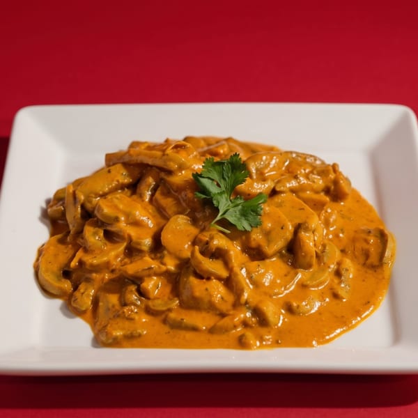 Mushroom dish in a rich orange sauce, garnished with cilantro on a white rectangular plate.