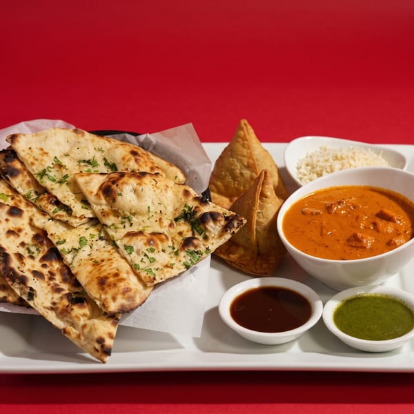 Indian meal with naan bread, samosas, butter chicken, rice, and two dipping sauces on a white platter.